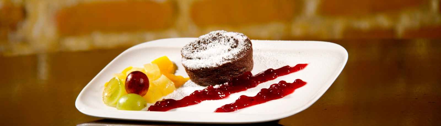 Kleiner Schokoladenkuchen mit flüssigem Kern auf Fruchtspiegel, dazu Obst