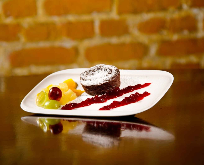 Kleiner Schokoladenkuchen mit flüssigem Kern auf Fruchtspiegel, dazu Obst